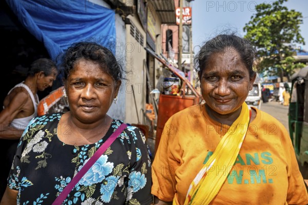 Two woman smiling at the camera on a sunny street in an urban setting