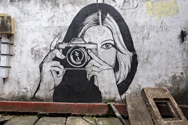 Black and white wall painting of a woman with camera in an urban environment