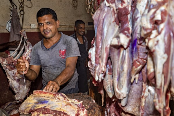 Butcher cuts meat in a shop while a colleague works in the background