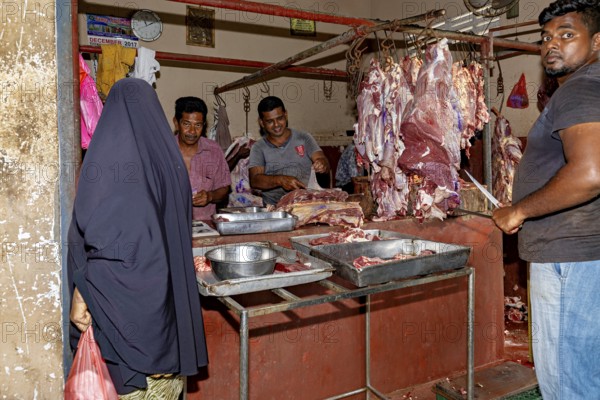 A butcher market with sellers and customers looking at and buying pieces of meat