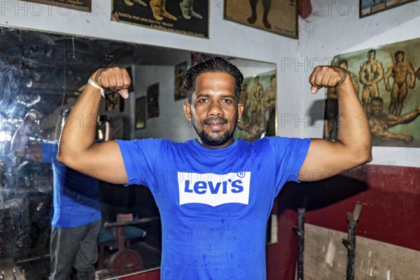 Man proudly shows off his muscle strength in a traditional fitness room