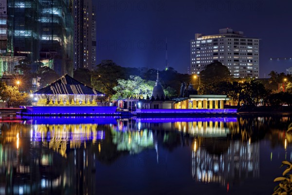 At night, a brightly lit temple is reflected in the calm waters of an urban lake, The Seema Malaka Temple in Colombo in Sri Lanka