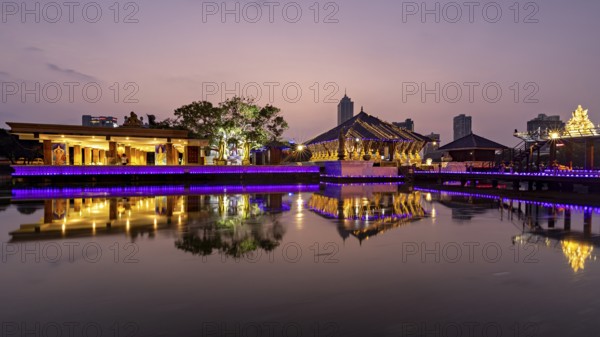An illuminated temple and city building are reflected in the tranquil lake at dusk, The Seema Malaka Temple in Colombo in Sri Lanka