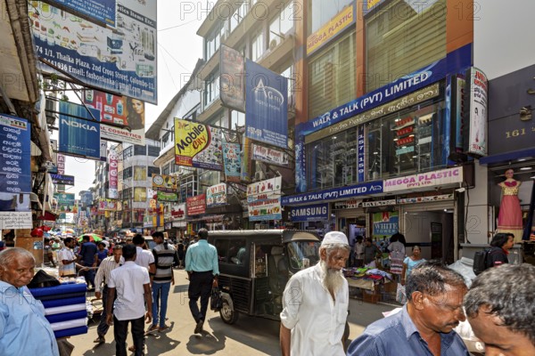 Populated street with shops and eye-catching advertising posters under clear skies, the hustle and bustle of Colombo city center in Sri Lanka