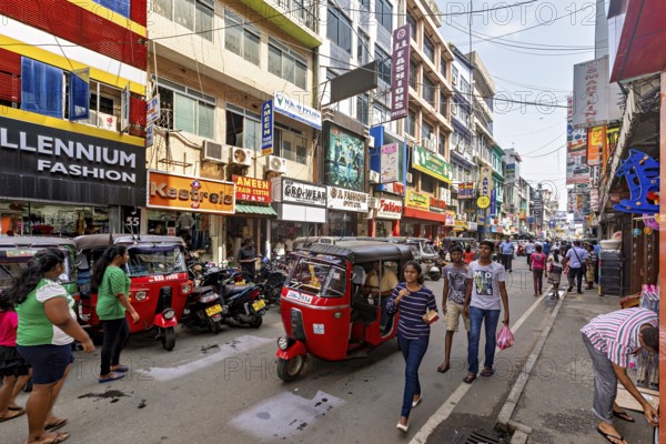Bustling shopping street with rickshaws and pedestrians flanked by colorful buildings, the hustle and bustle of Colombo city center in Sri Lanka