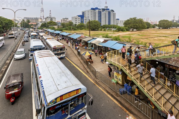 City street with buses and busy market on the right, buildings in the background, buses on the road in Colombo in Sri Lanka