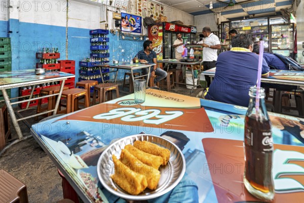 Casual snack with colorful tables and chairs, relaxed atmosphere, food and drinks on the tables, people in a simple restaurant in Colombo in Sri Lanka