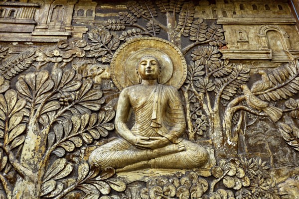 Relief depiction of Buddha in meditation surrounded by plants and architectural details, statues of gods in the temples of Colombo in Sri Lanka