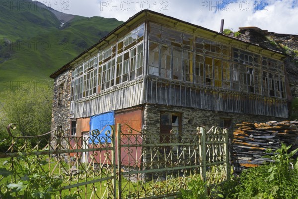 Old-fashioned house with a glass veranda against a mountain backdrop. Rustic atmosphere in green landscape, traditional house, Ushguli, Ushguli, Shibiani district, Zhibiani, Upper Svaneti, Svaneti, Georgia