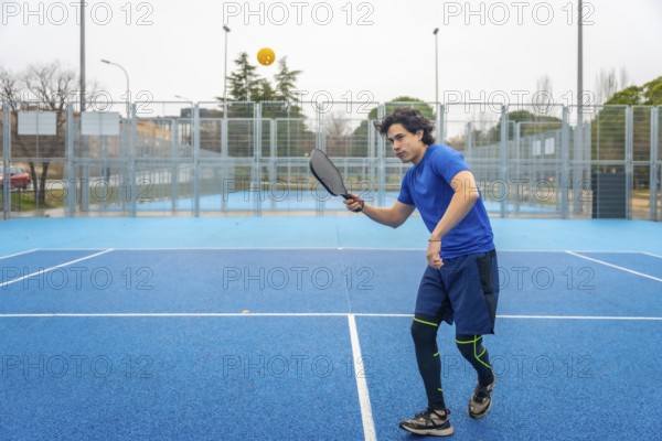 Athlete wearing athletic clothing using a paddle to hit a pickleball during an intense match, demonstrating skill and agility on the brightly colored blue court
