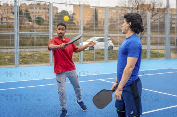 Young men enjoying a game of pickleball, one hitting the ball with a paddle on a vibrant blue court, embodying an active lifestyle and camaraderie in an outdoor setting