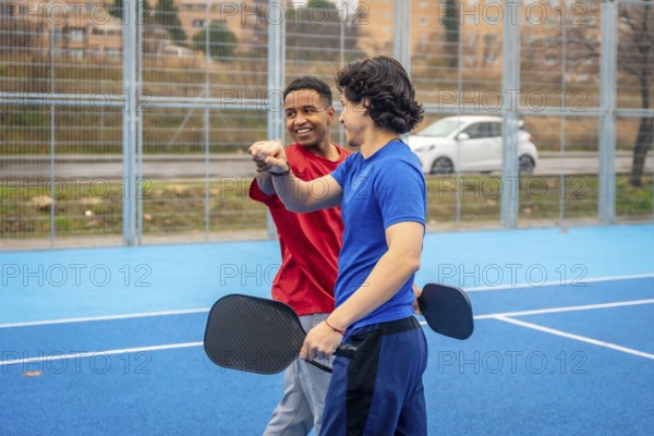 Two diverse male athletes fist bumping on an outdoor blue pickleball court, symbolizing collaboration, camaraderie, and team spirit after a game or practice session