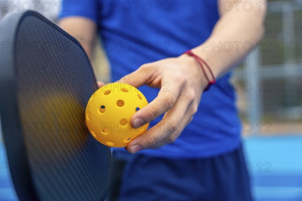 Hands holding a yellow pickleball and paddle on an outdoor court, poised to serve or dinkclose up capturing active lifestyle, sport, leisure, and summer fitness readiness