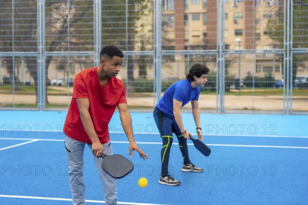 Young men poised on a bright blue court with paddles and ball, ready for an outdoor pickleball matchfitness, teamwork and active leisure captured in motion and camaraderie