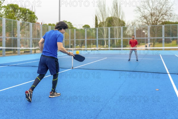 Two male athletes playing an intense pickleball game on a vibrant blue court, hitting the ball over the net with full concentration during a competitive match