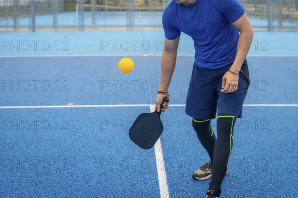 Man strikes a pickleball with his paddle on a vivid blue outdoor court, showcasing athletic movement, focus and active lifestyle during competitive recreational play