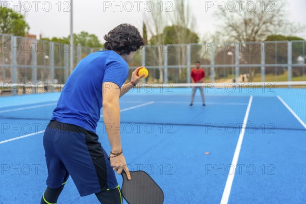 Pickleball player poised to serve on a blue outdoor court facing an opponent, highlighting athletic fitness, leisure competition, quick movement and social sportsmanship