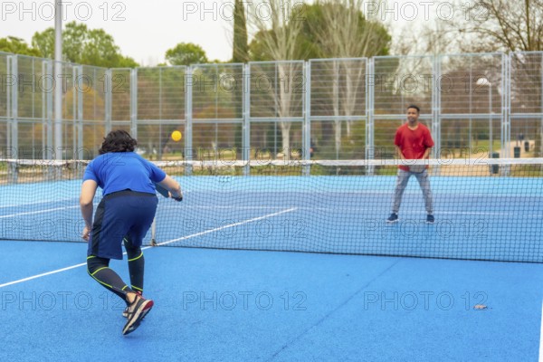 Two men compete in an energetic outdoor pickleball match on a bright blue court, volleying with paddles and enjoying active recreation, fitness and friendly competition