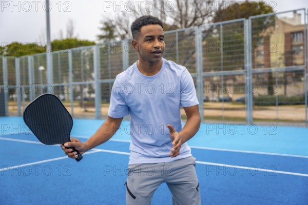 Young man standing on a blue pickleball court, holding a paddle and preparing to hit the ball, actively engaged in a fun, energetic racket sport and healthy lifestyle