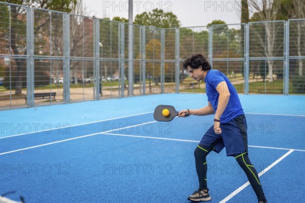 Young man in sportswear hitting a pickleball with a paddle on an outdoor blue court, focused and energetic during competitive play showcasing fitness and active lifestyle