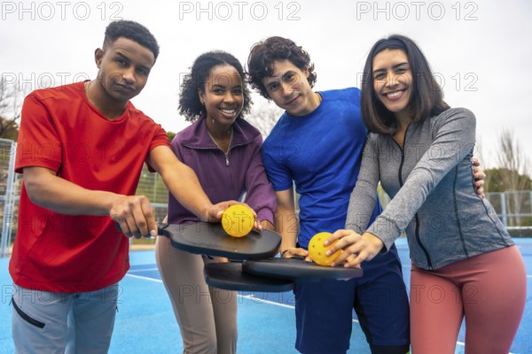 Four happy diverse friends on a bright blue pickleball court, smiling at the camera and holding paddles with a pickleball, promoting sport, friendship, and an active lifestyle