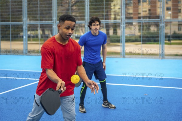 Young diverse men playing pickleball, engaging in active recreation and enjoying the outdoor sports court, developing skills and teamwork in a modern competitive activity