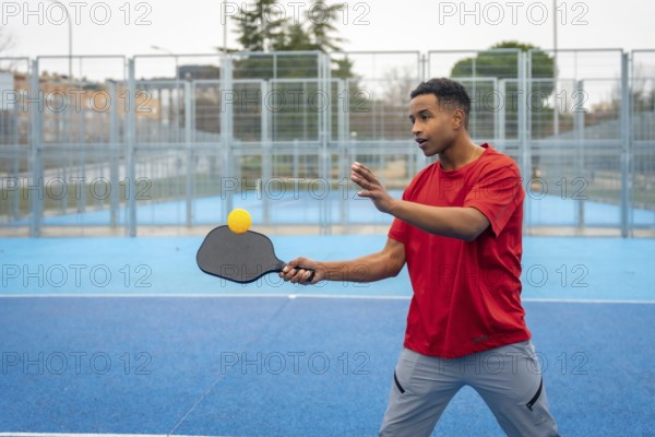 Young man concentrating on returning the ball during a pickleball game on a bright blue outdoor court, engaging in a healthy active lifestyle and recreational sport