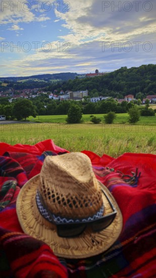 A straw hat on a blanket with a view of a village against a cloudy sky, view of Rosenberg Fortress, Burg, Upper Franconia