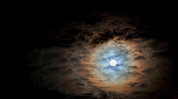 Full moon surrounded by dramatic, colorful clouds in the night sky