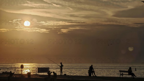 Sunset at sea with silhouettes of people including a fisherman