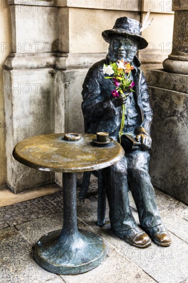 Life-size bronze sculpture as a memorial to Piotr Skrzynecki, Polish choreographer and cabaret director sitting at a coffee table, rynek with cloth halls, from 13th century, main market, city landmark, Krakow, Poland