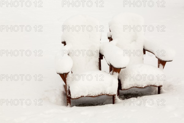 Two brown stained wooden Adirondack chairs covered in freshly fallen winter like snow in public park in late autumn, Quebec, Canada