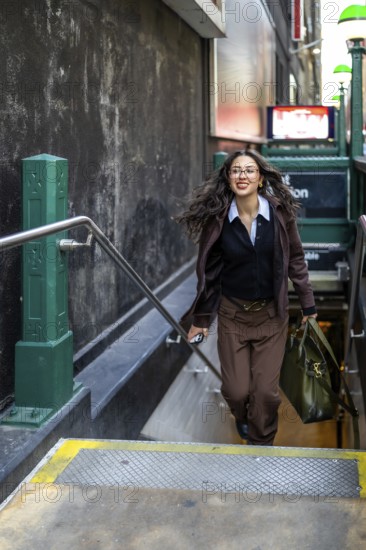 Young businesswoman with a confident smile and flowing hair, carrying a professional bag and a phone, making her way up the steps from a new york city subway station during her daily commute