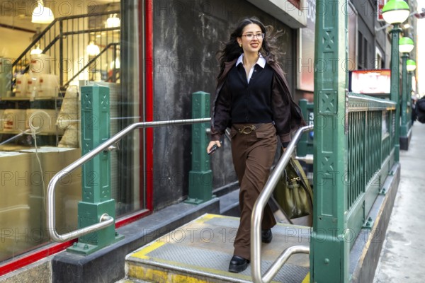 Young businesswoman with a confident smile walking up the stairs from a subway station entrance, holding a phone and bag, and navigating the urban environment of new york city