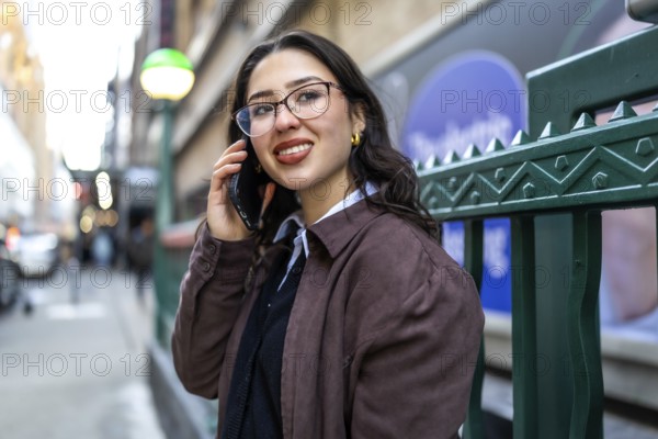 Young businesswoman standing in new york city, actively communicating on her mobile phone while smiling confidently, embodying urban professional mobility and connection