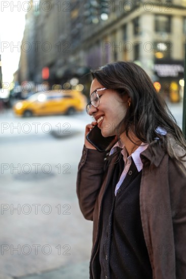 Young female executive communicating on a mobile phone, smiling and engaging in a casual conversation while walking through the bustling urban streets of manhattan during the day