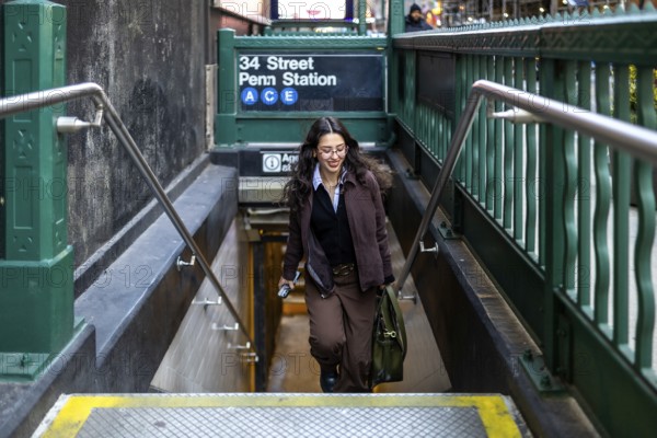 Young female executive with a satchel bag going down the stairs of the 34 street penn station a c e subway entrance in manhattan, wearing a jacket and carrying a phone, ready for her daily commute