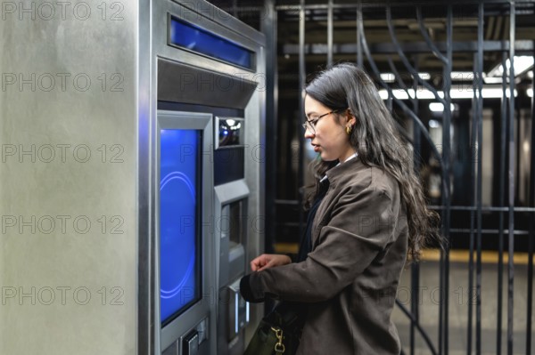 Young businesswoman with glasses and sleek dark hair interacting with a subway ticket machine, managing her urban commute and digital transaction in a bustling city environment