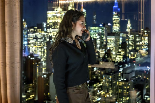 Young businesswoman in a high rise office talks on her phone at night, overlooking manhattan's illuminated skyline confident executive connecting globally, planning and leading