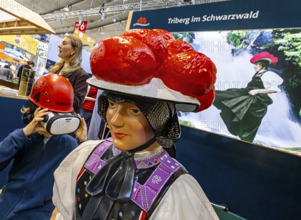 Tradition and progress. A young trade fair visitor wearing 3D glasses next to a model of a woman wearing traditional traditional costume and a Black Forest Bollenhut. Caravan — Motor — Tourism trade fair in Stuttgart. According to the exhibition organizer, CMT is the world's largest public trade fair for tourism and leisure. Stuttgart, Baden-Württemberg, Germany
