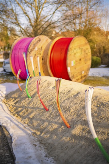 Colourful cables stick out of a snow hill, behind them colorful rolls of cable in winter light, fibreglass groundbreaking, Freudenstadt, Germany
