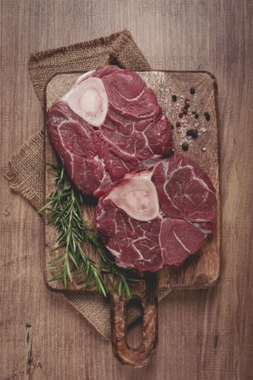 Knuckle on the bone, raw meat for ossobuco, on a wooden chopping board, with a sprig of rosemary, and spices, top view, no people