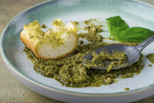 On a platter is a pesto sauce made from fresh basil, with a slice of bread and a spoon on a plate. The pesto sauce looks creamy and green, and the bread is partially eaten