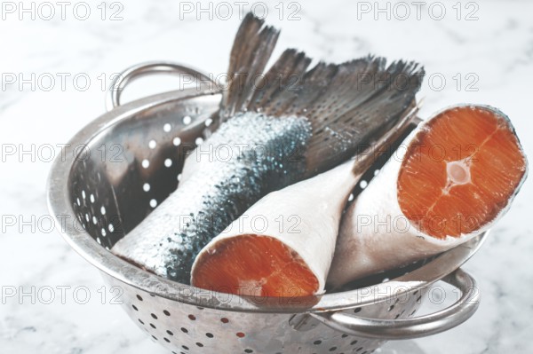 Fish tails are placed in a colander on a marble counter. The colander allows water to drain away from the fish. The fish looks fresh and clean, ready for cooking or preparation