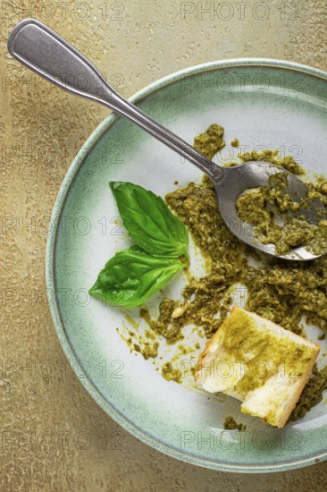 On a platter is a pesto sauce made from fresh basil, with a slice of bread and a spoon on a plate. The pesto sauce looks creamy and green, and the bread is partially eaten