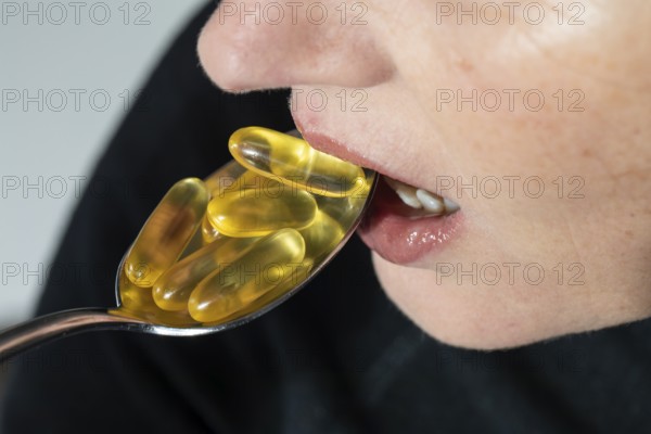 Face of a woman taking many omega capsules from a spoon