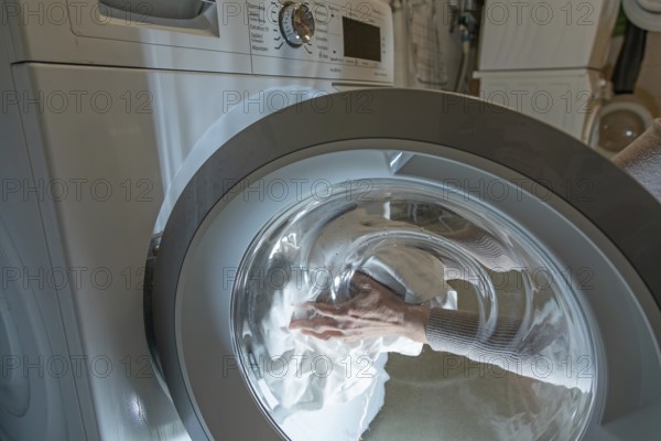 Woman loading clothes into a washer for cleaning. Germany