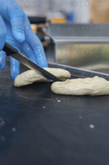A person in gloves cuts dough with a knife in the bakery, baking rolls, Haselstaller Hof, Gechingen, Germany