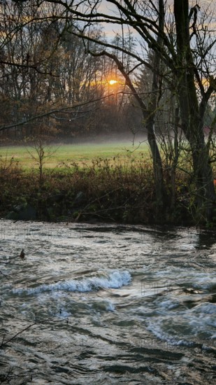 A quiet autumn evening on the river flowing through a forest as the sun sets behind the trees, Frankenwald nature park Park, Germany