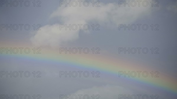A vivid rainbow against a blue sky with light clouds, Rennsteig, Germany